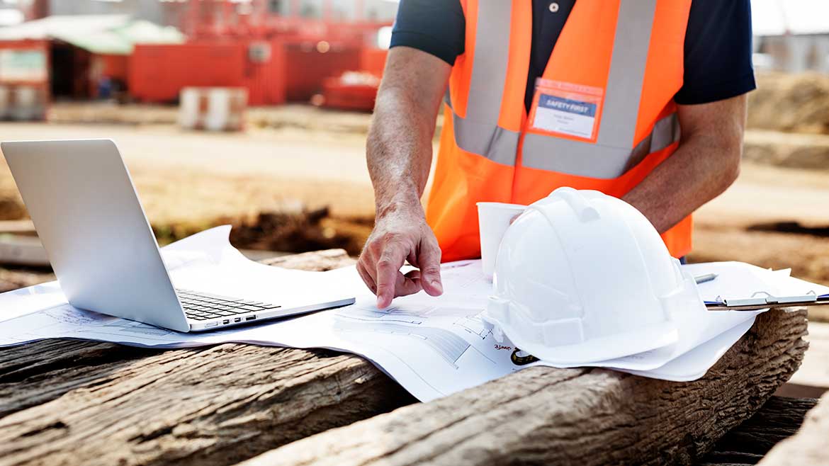 A construction worker is pointing to some papers.