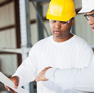 Two men in hard hats looking at a paper.