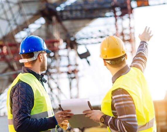 Two men in hard hats and vests talking.