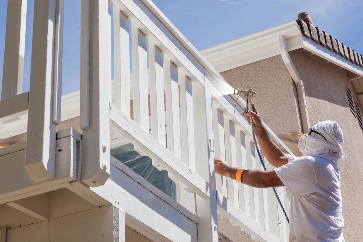 Painter spray-painting white deck railing.